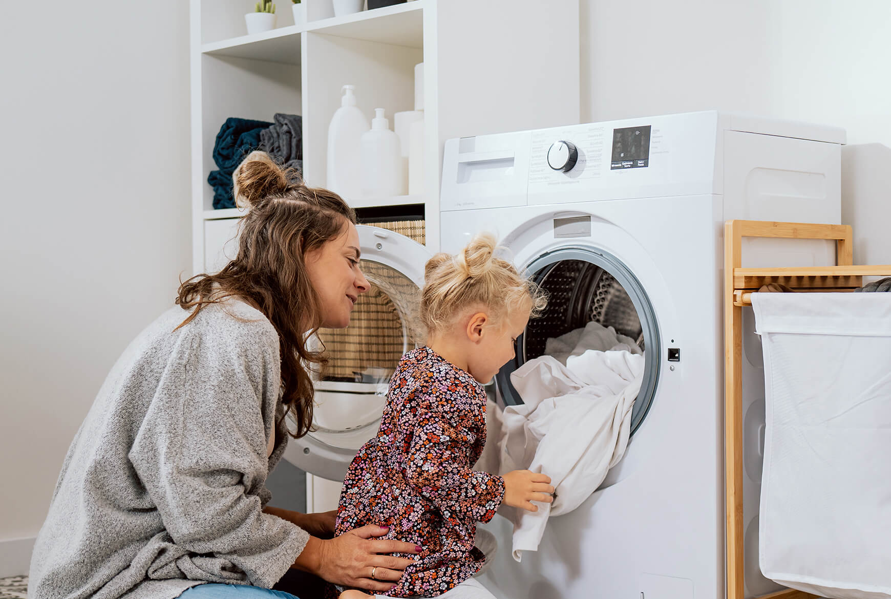 Une maman avec une petite fille qui met des vêtements dans une sécheuse