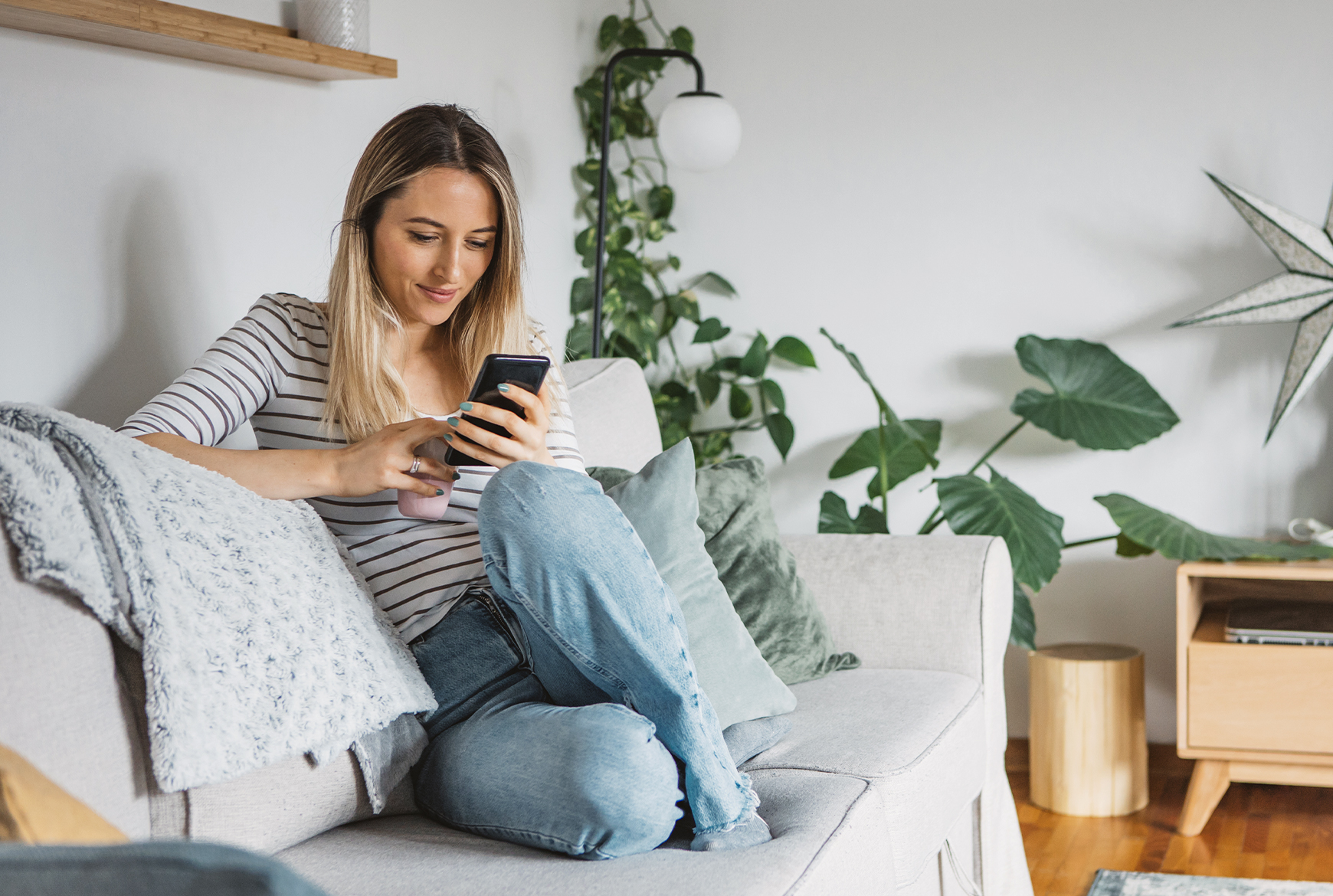 Une femme regarde son cellulaire assise sur son divan