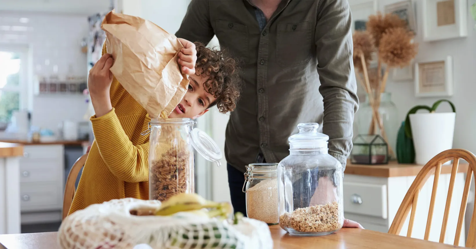 A child pouring dry food into a glass jar