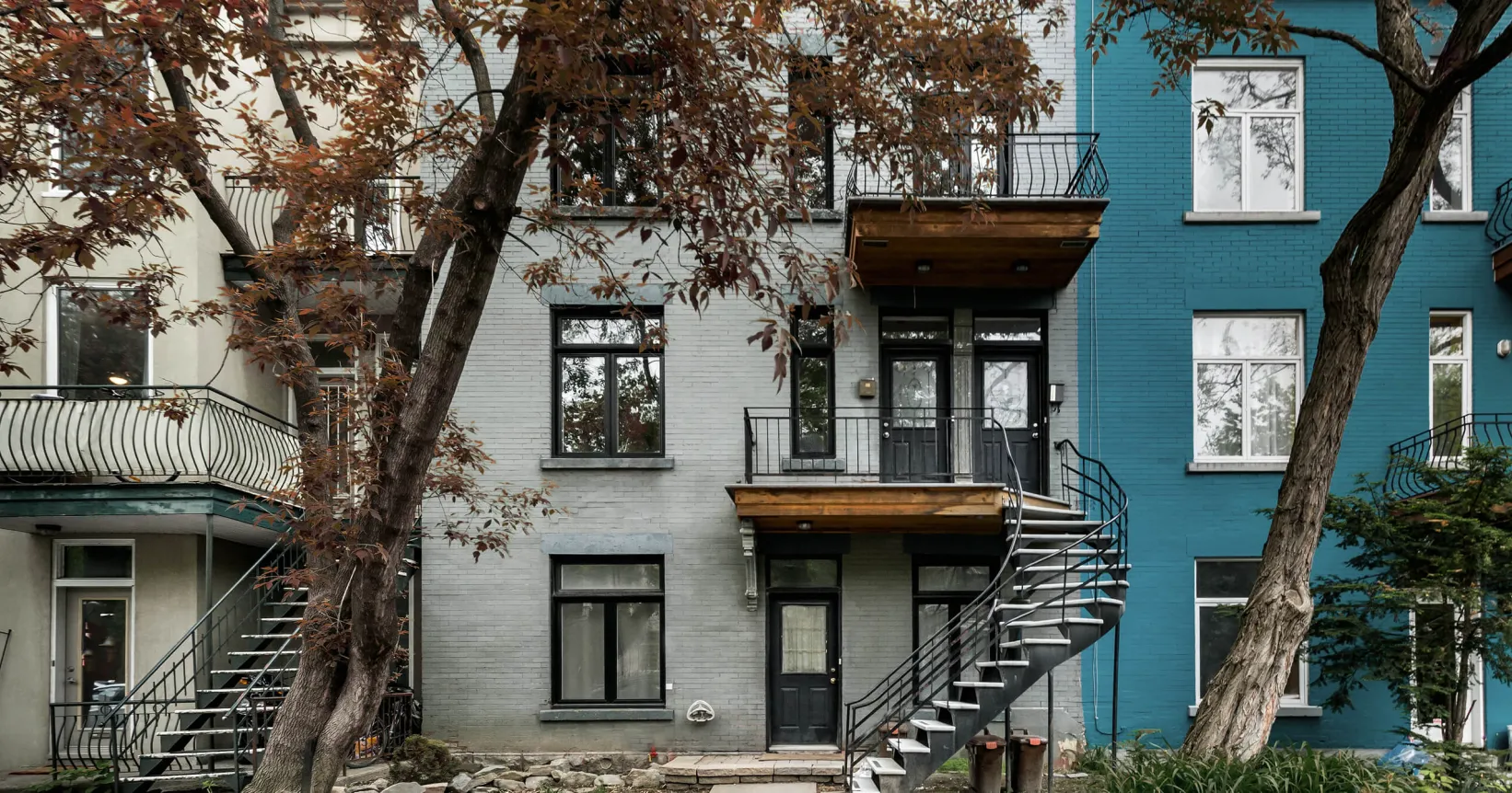 Façade d'immeubles gris et bleu avec des escaliers et un arbre devant