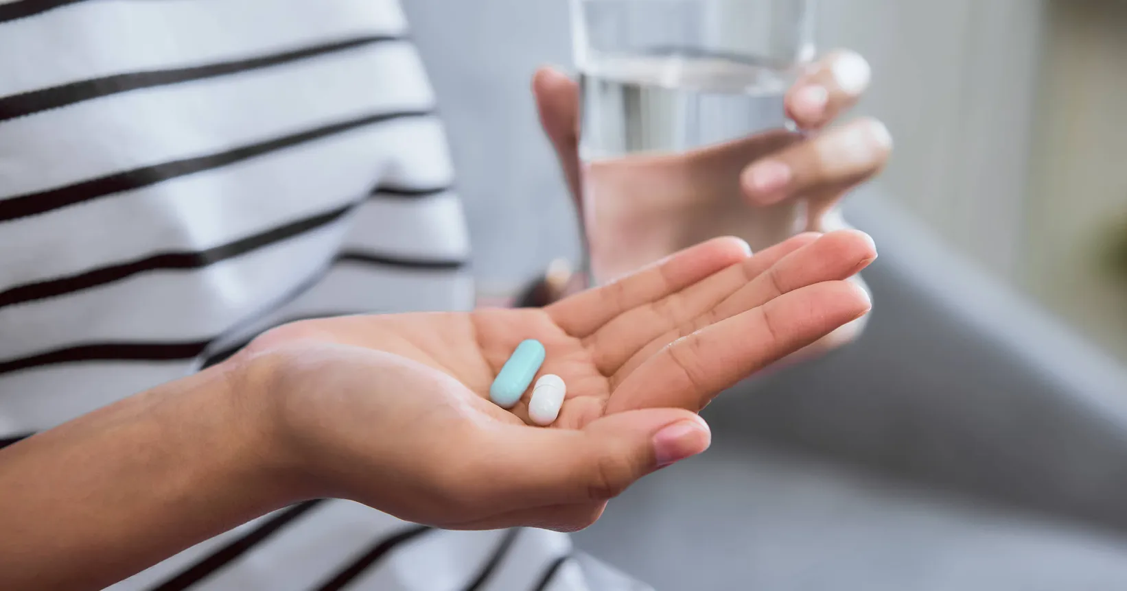 Une main avec des médicaments et un verre d'eau