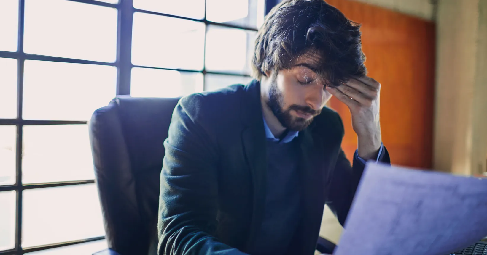 Un homme se tient la tête devant son ordinateur portable