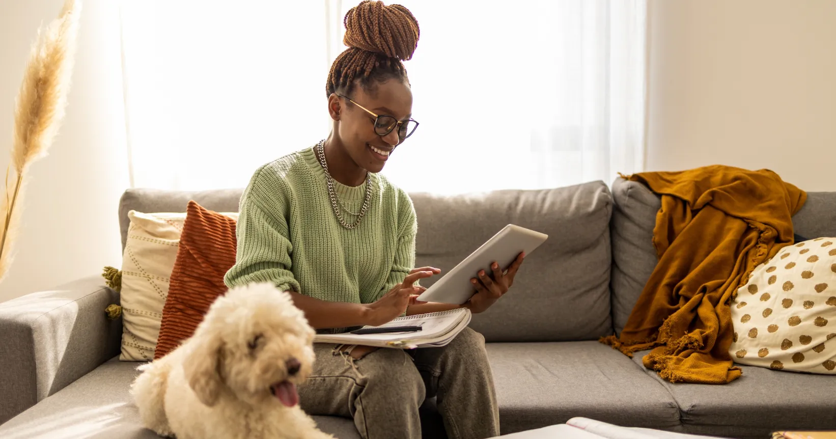 Une femme assise sur son divan consulte une tablette électronique