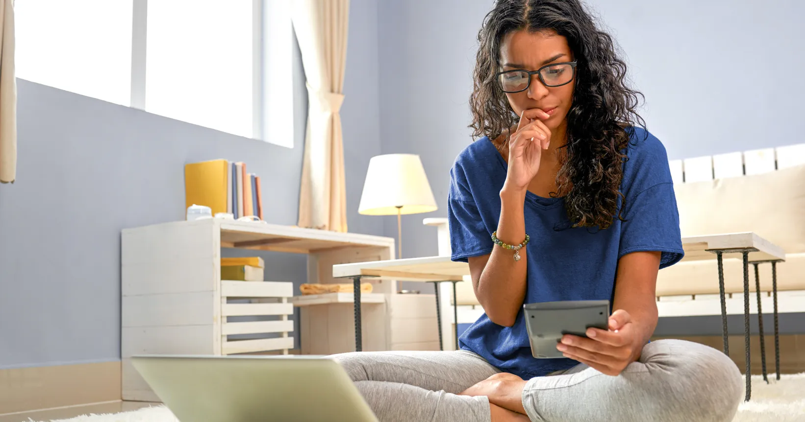 Une femme regarde une calculatrice devant son ordinateur portable