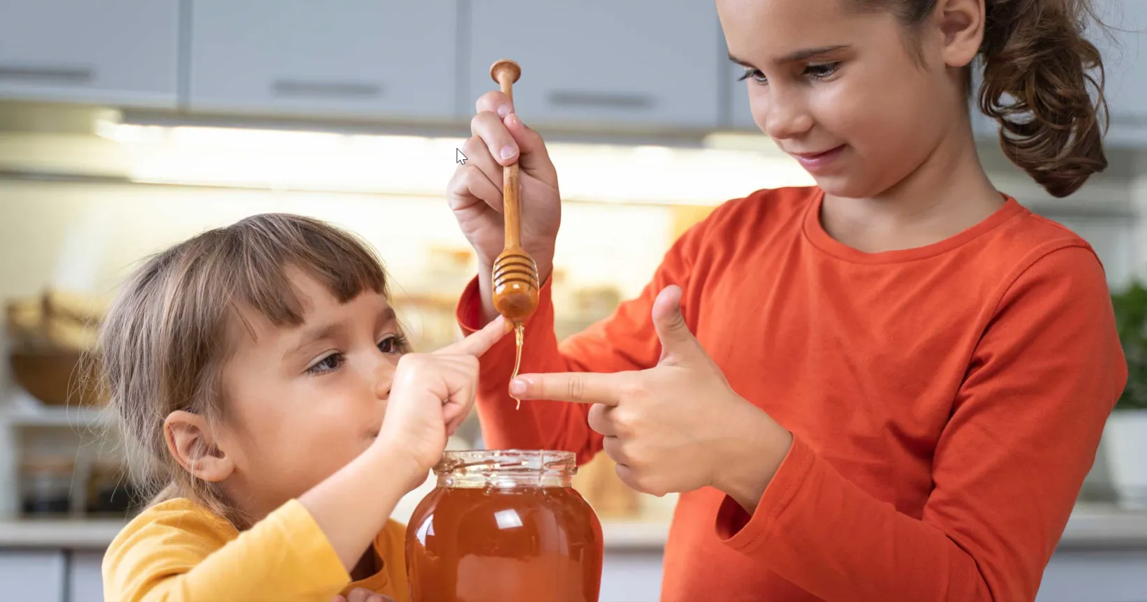 Deux enfants versant du miel dans un bocal en verre
