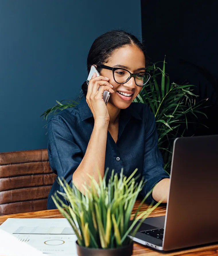 Person seated at a computer, holding a phone to their ear
