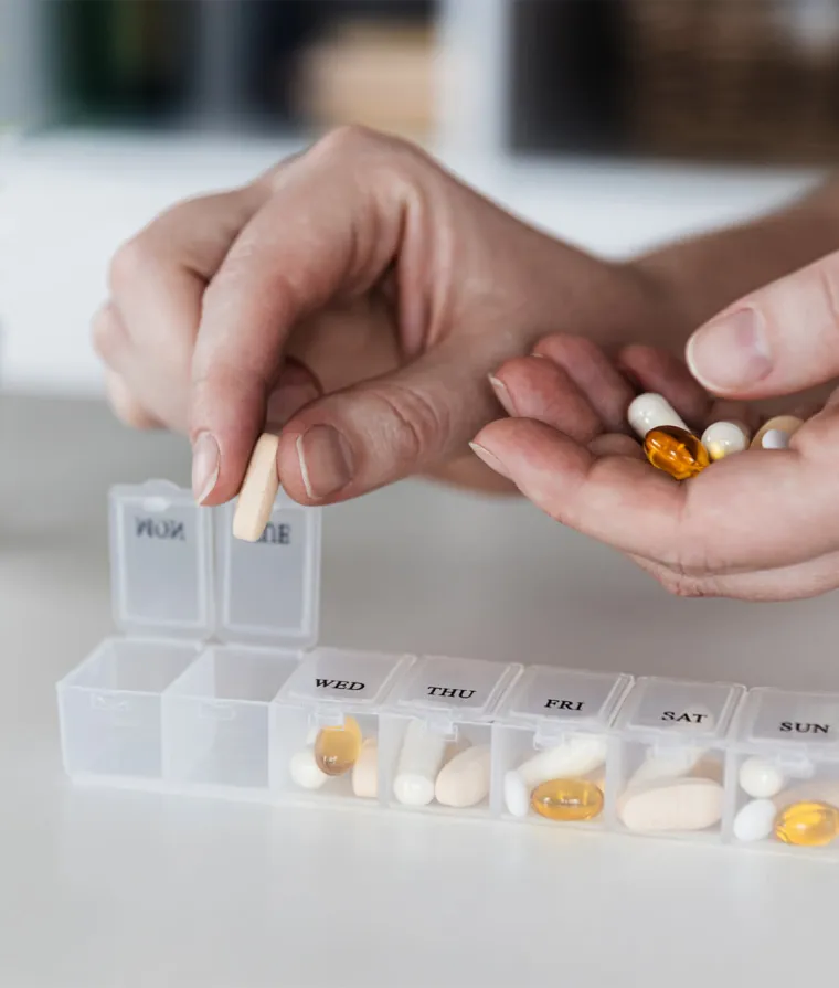 Gros plan sur les mains d'une personne qui met des médicaments dans une boite à comprimés 