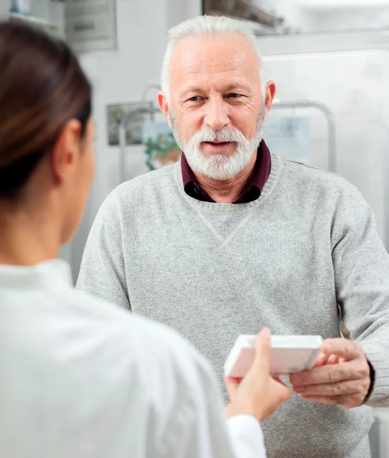 Un monsieur âgé se fait donner des médicaments par une pharmacienne