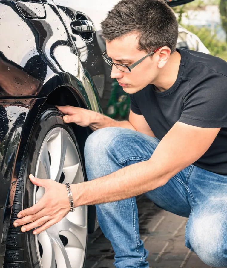 Un jeune homme inspecte les pneus d'une voiture