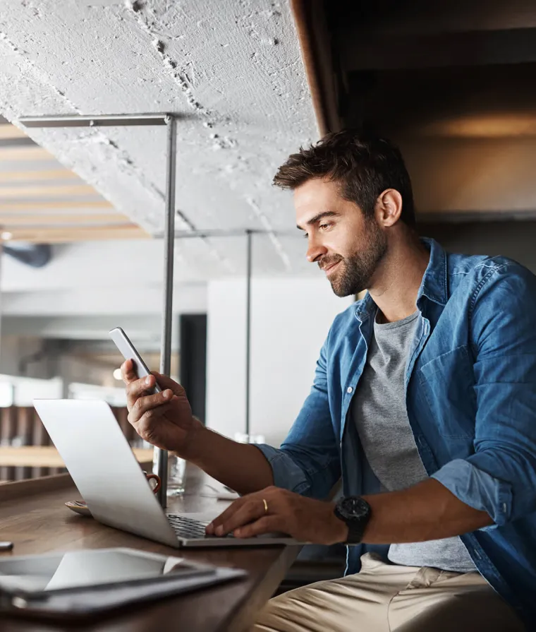 Un homme consulte son téléphone portable devant son ordinateur