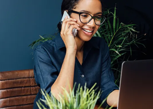 Person seated at a computer, holding a phone to their ear