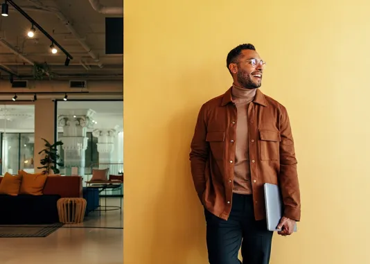 Person standing holding a laptop, looking off to the side