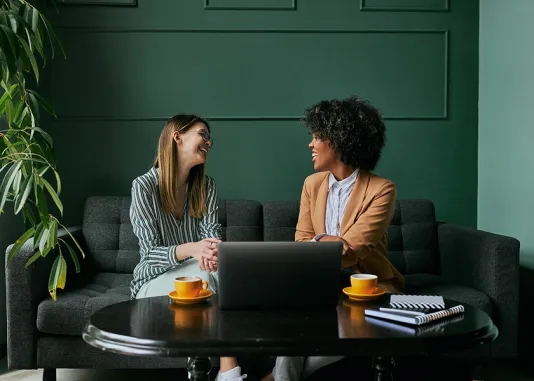 Two people seated talking in front of a computer